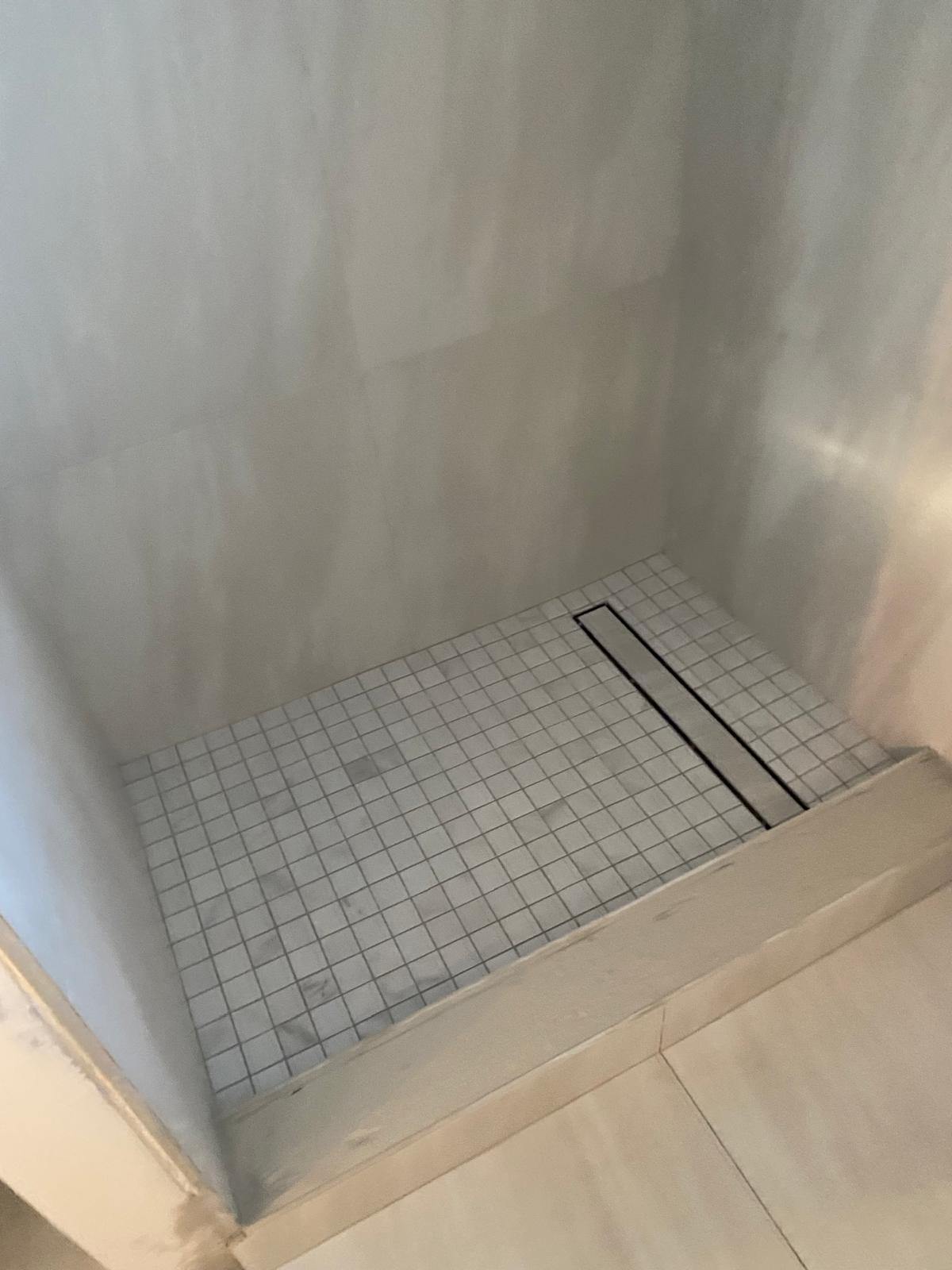 Linear drain set into a sloped mosaic shower pan during a Tampa plumbing and tile job
